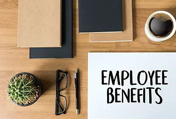 Desk with paper notepads, coffee, pen and paper displaying employee benefits. 