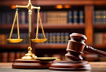 Gold scales of justice and gavel sit on table with law books in background.