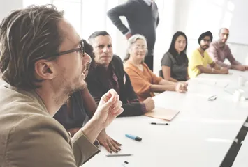 Image: A group of people speaking around a conference room table.