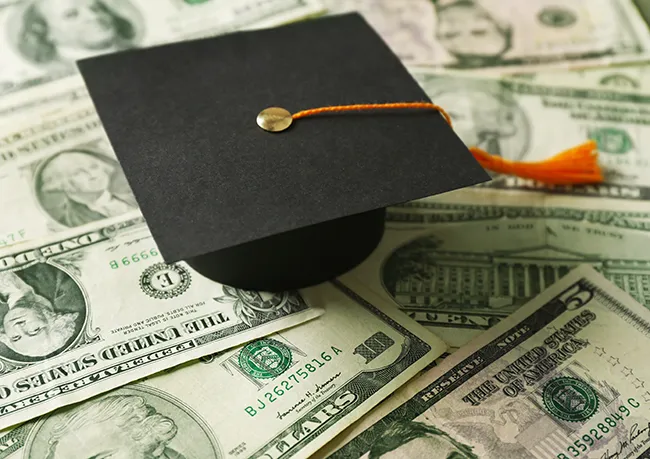 Graduation cap sitting on top of U.S. currrency.