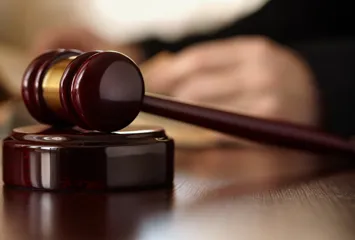 A gavel on a table with a judge's hand in the background.