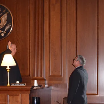 Judge Castel swears in a witness in a dimly lit courtroom. Small table lamps provided the necessary light to conduct proceedings during the week of the storm.