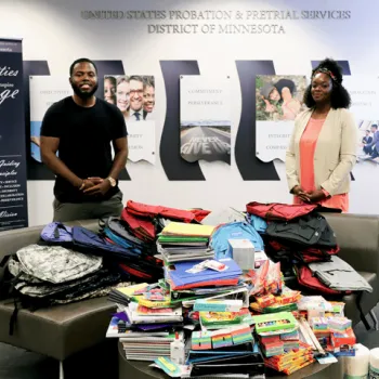 A man and a woman pose in front of the school supplies collected for local school areas.