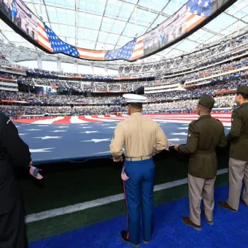 New citizens and service members stretch the American flag across the football field.